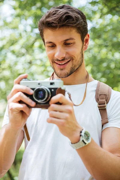 Cheerful man with backpack taking pictures using vintage camera outdoors