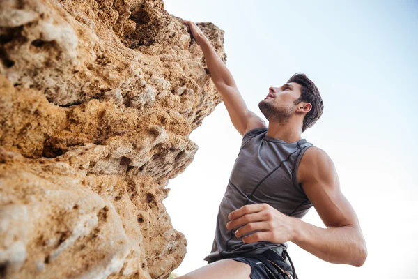 Man reaching for a grip while he rock climbs