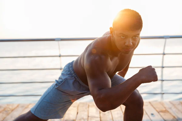 Muscular african man athlete warming up and exercising on pier