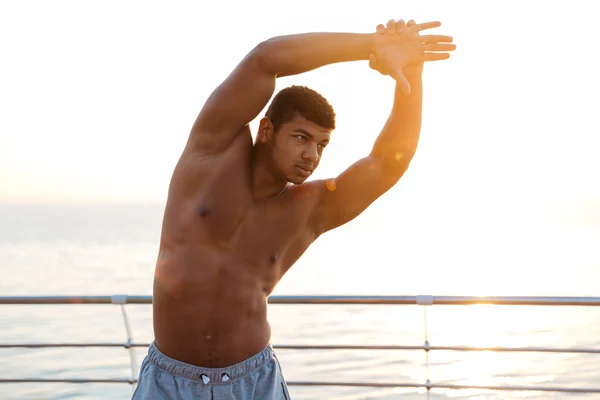 Handsome muscular african man athlete doing stretching exercises on pier