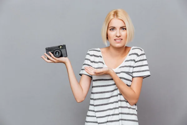 Confused blonde young woman holding old vintage photo camera