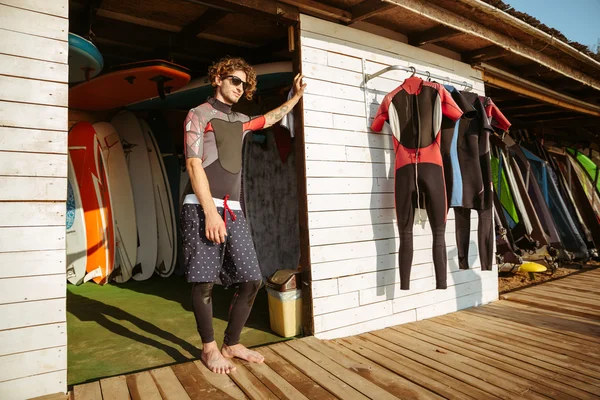 Curly man in swimsuit standing at the beach hut