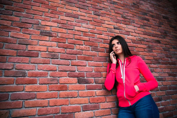 Young woman talking on the phone over brick wall