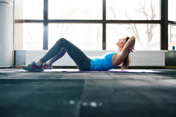 Young woman lying on the yoga mat and doing fitness exercise