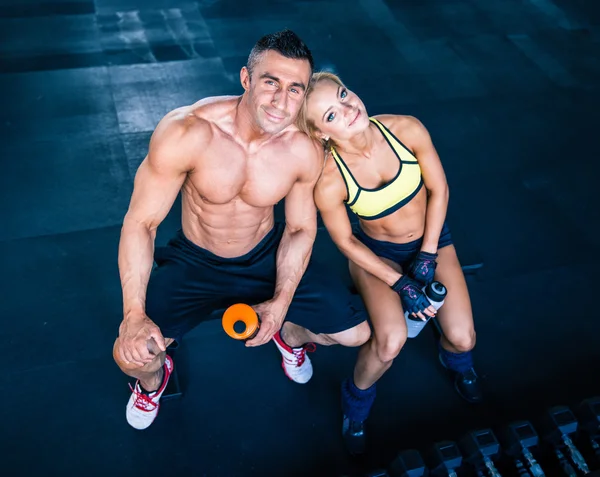 Muscular man and woman resting on bench at gym