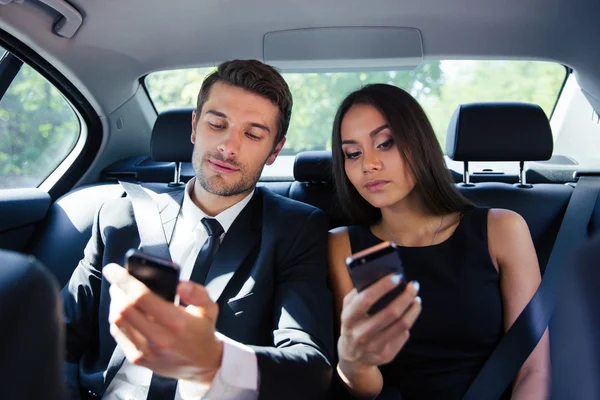 Businessman and businesswoman using smartphone in car