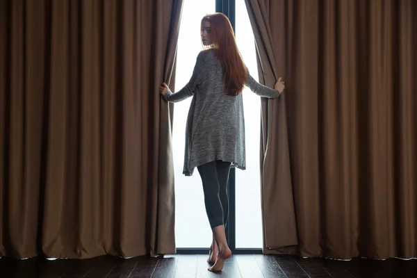 Relaxed  woman opening curtains and looking back