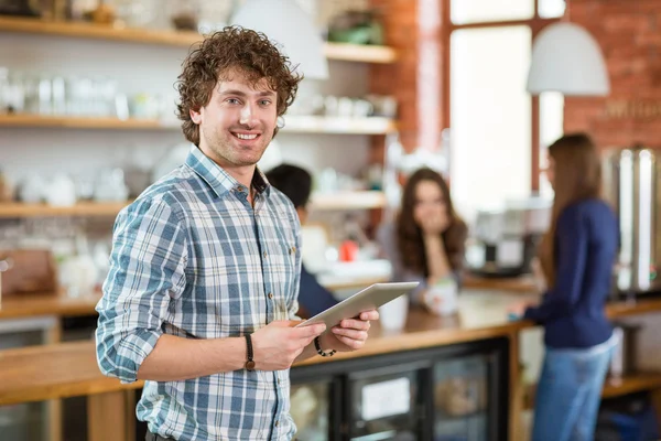 Cheerful curly young guy using tablet in cafe