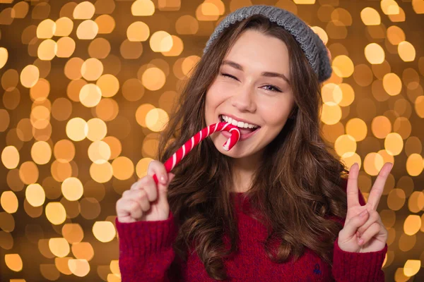 Pretty smiling woman biting christmas candy cane over sparkling background