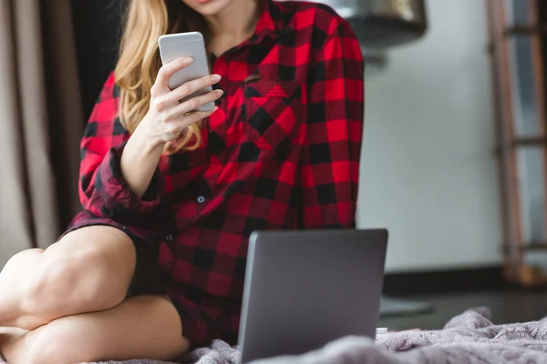 Beautiful woman in checkered shirt using cell phone and laptop