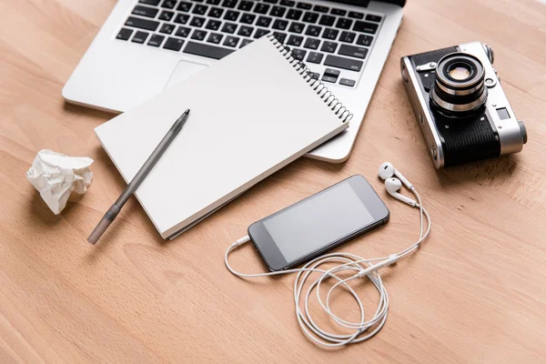 Laptop, vintage camera, mobile phone, earphones and notebook with pen