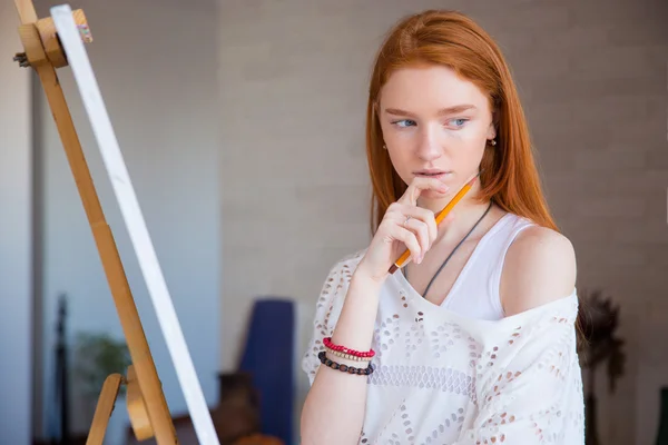 Pensive attractive female artist thinking near easel in drawing class