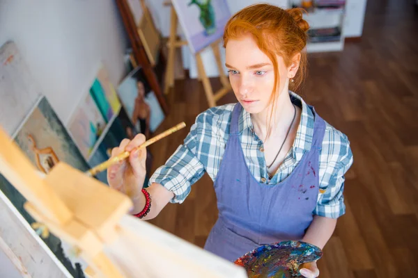 Concentrated woman painter holding art palette and painting on canvas