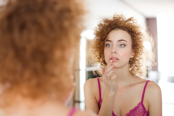 Sensual beautiful woman with curly red hair looking in mirror