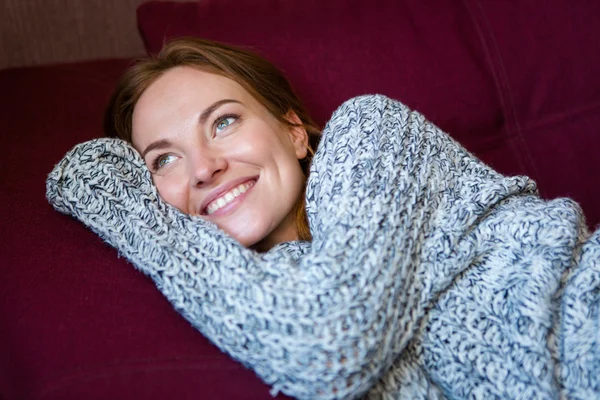 Portrait of cheerful woman in knitted sweater lying on couch