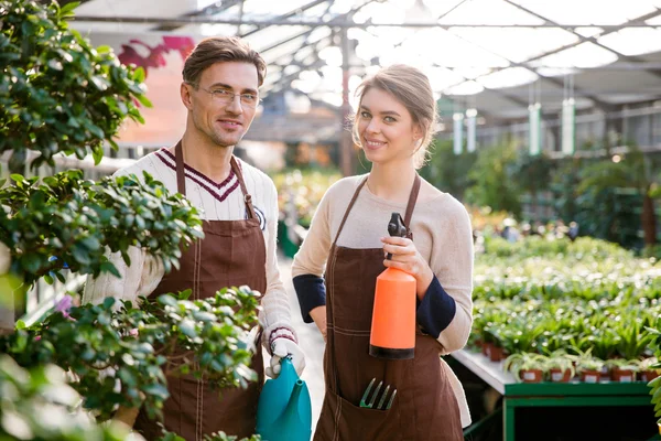 Happy gardeners holding watering can and pulveriser for spraying flowers