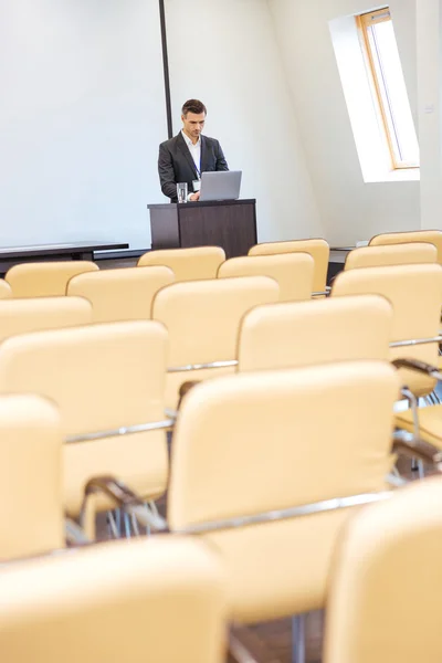Pensive businessman standing and using laptop in empty meeting hall