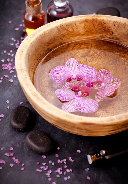 Spa set. Orchid flowers in a bowl with water, zen stones, and massage oils