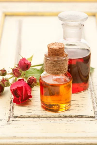 Rose essential oil and rose flowers on a white background