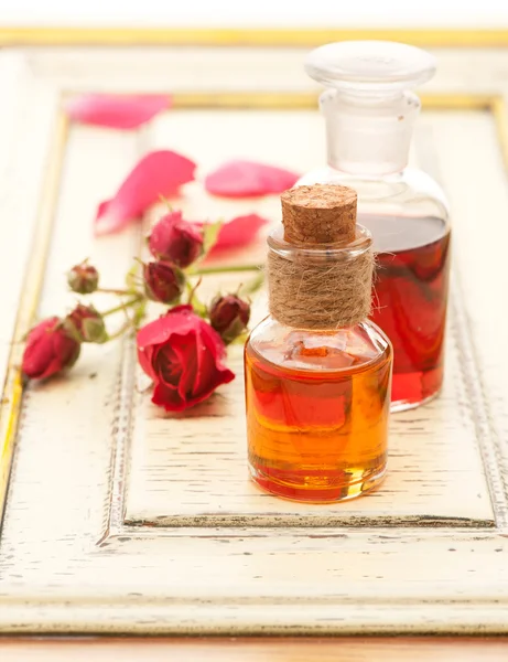 Rose essential oil and rose flowers on a white background