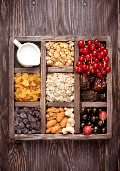 Granola, berries, nuts, dried fruit and milk. Healthy food in wooden box. Top view