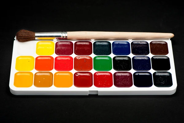 The palette of watercolor paints and brushes on a black background
