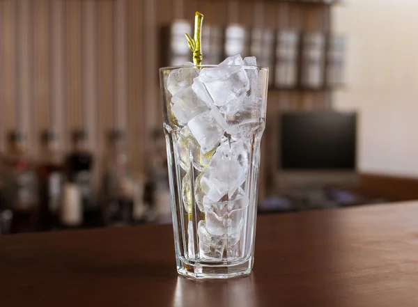 Highball glass with ice and a yellow tube on the wooden bar
