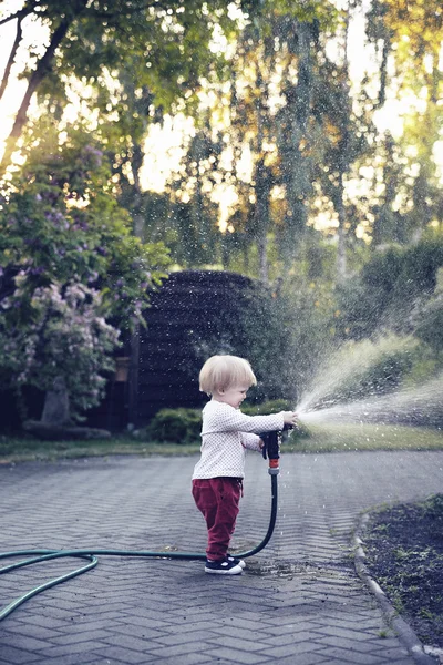 Baby girl watering the garden with hose