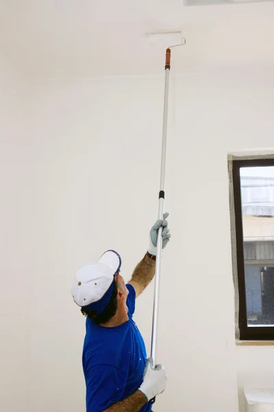 Worker paints the ceiling with an anchor roller