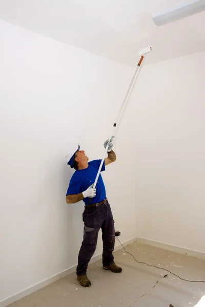 Worker paints the ceiling with an anchor roller