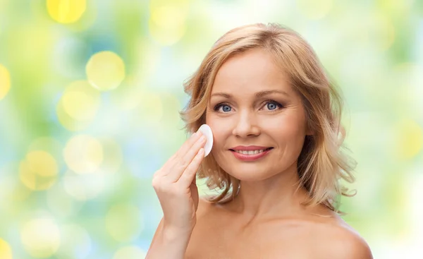 Happy woman cleaning face with cotton pad