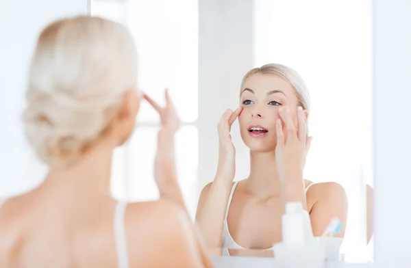 Happy woman applying cream to face at bathroom