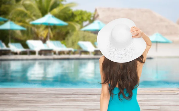 Woman in swimsuit and sun hat from back over beach