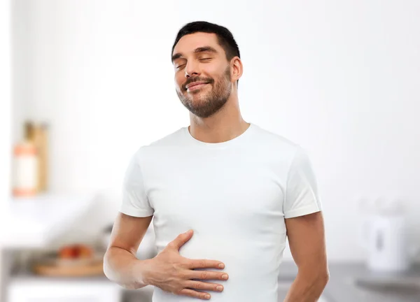 Happy full man touching tummy over kitchen