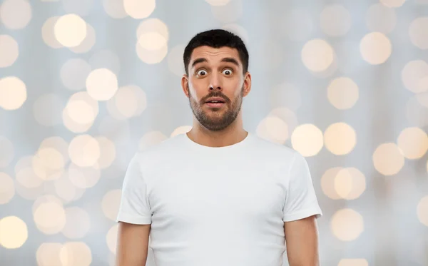 Scared man in white t-shirt over lights background
