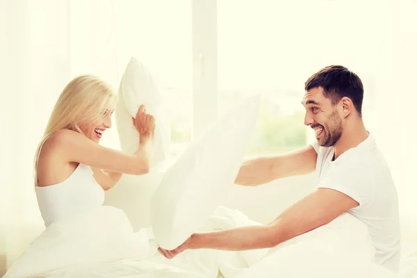 Happy couple having pillow fight in bed at home