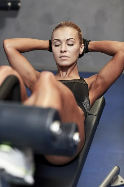 Woman flexing abdominal muscles on bench in gym