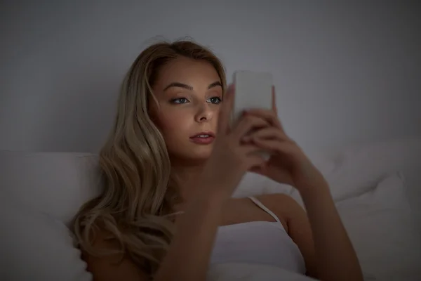 Young woman with smartphone in bed at home bedroom