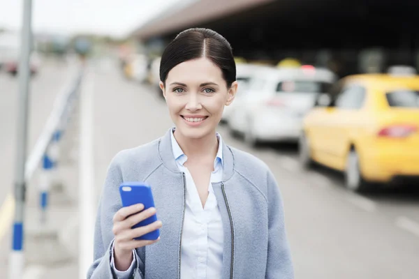 Smiling woman with smartphone over taxi in city