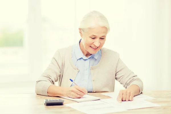 Senior woman with papers and calculator at home