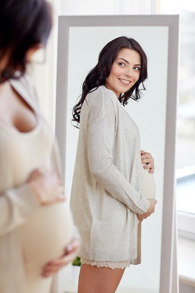 Happy pregnant woman looking to mirror at home