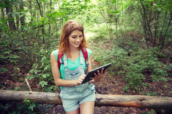 Happy woman with backpack and tablet pc in woods