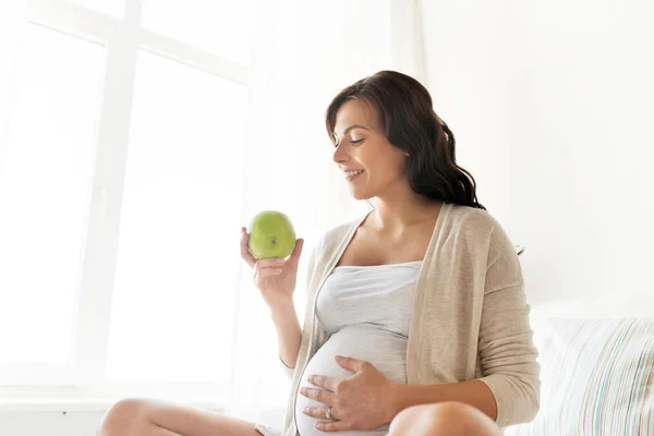Happy pregnant woman eating green apple at home