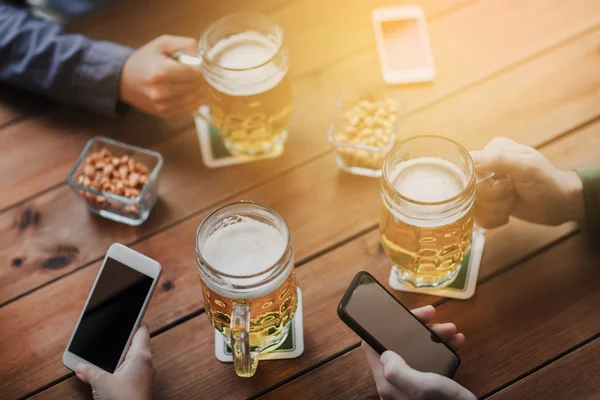 Close up of hands with smartphones and beer at bar