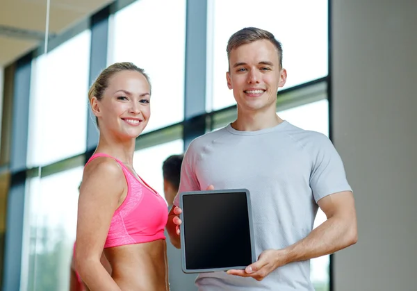 Smiling young woman with personal trainer in gym