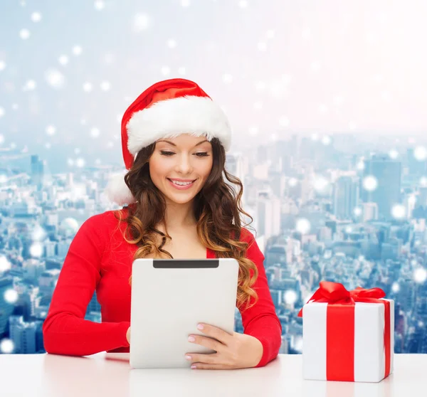 Smiling woman in santa hat with gift and tablet pc