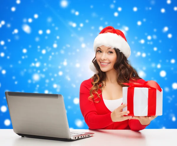 Smiling woman in santa hat with gift and laptop