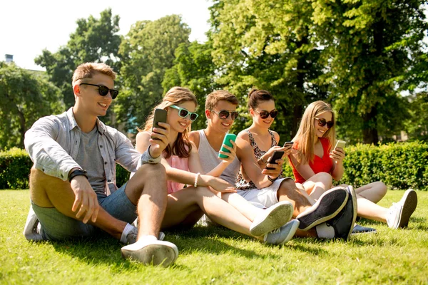 Smiling friends with smartphones sitting on grass