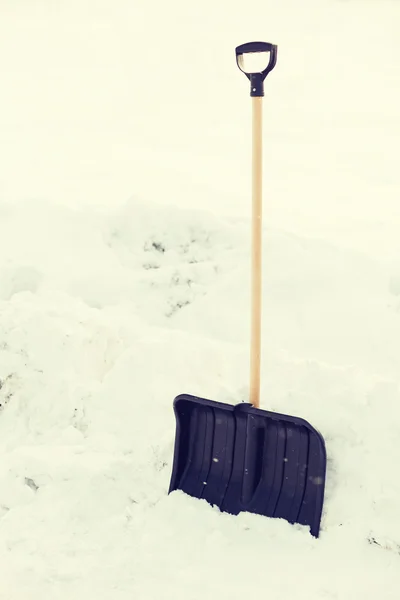 Black snowshowel with wooden handle in snow pile