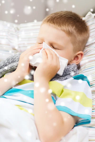 Ill boy blowing nose with tissue at home
